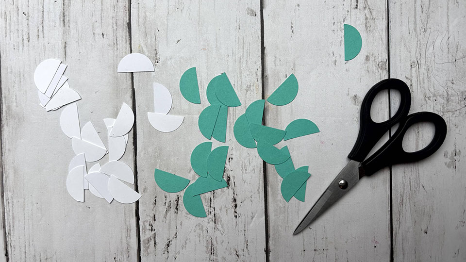 Découpe de cercles en papier blanc et vert en deux avec des ciseaux pour motif géométrique carte DIY homme