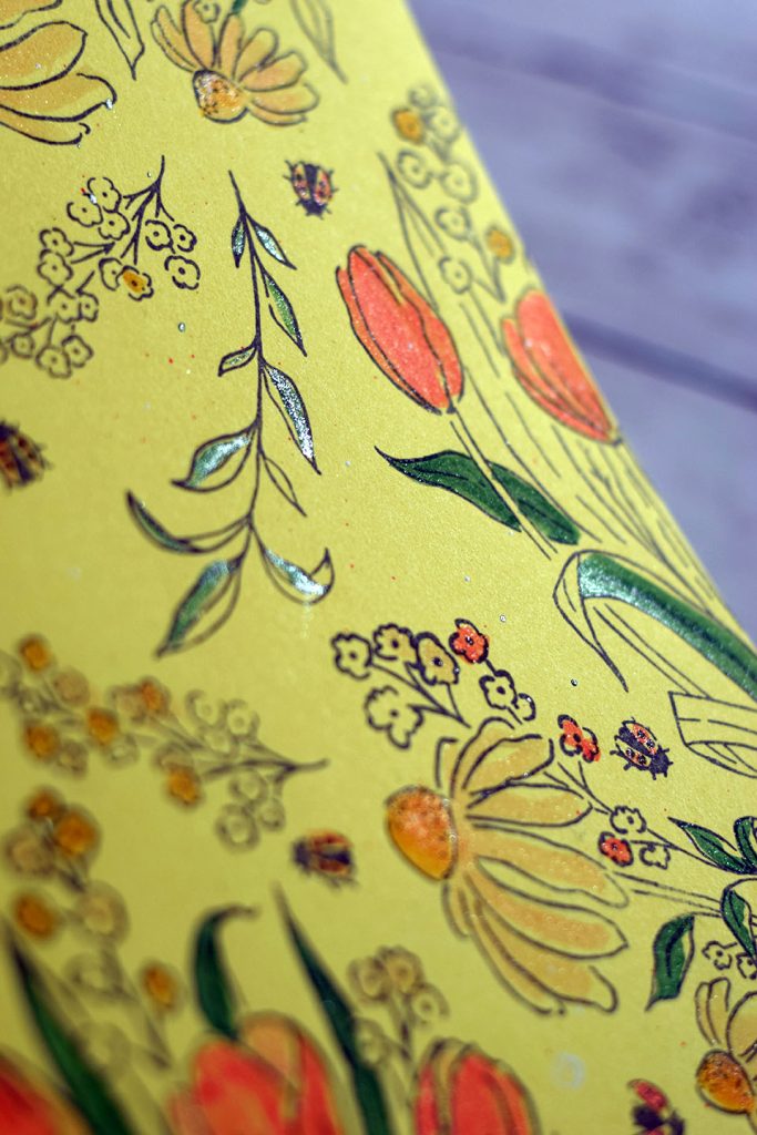 Tampon fleuri sur du papier jaune et colorisation des motifs avec effets de brillant