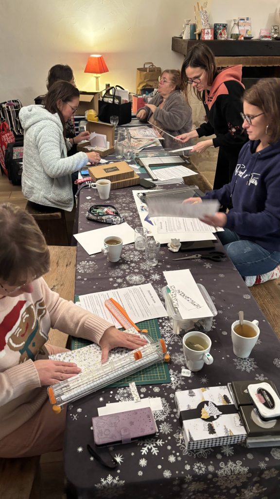 Participantes concentrées sur leurs projets scrapbooking autour d'une longue table lors du week-end scrap à La Bergerie